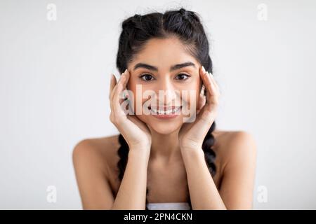 Hautpflegekonzept. Wunderschöne Junge Indische Frau, Die Das Gesicht Berührt Und Die Kamera Anlächelt Stockfoto