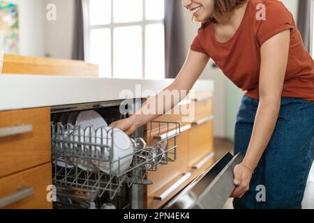 Wunderschöne junge araberin, die in der modernen Küche eine Spülmaschine benutzt Stockfoto