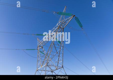 Nahaufnahme des oberen Abschnitts eines Hochspannungs-Pylons mit Stromleitungen vor einem blauen Himmel Stockfoto