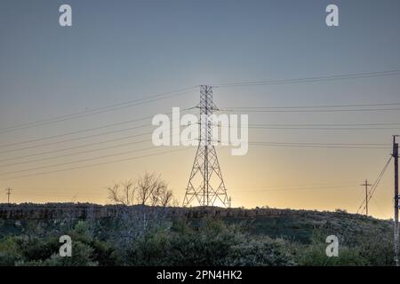 Hochspannungsleitungen auf einem Hügel bei Sonnenuntergang mit Sonnenuntergang hinter dem Pylon, Hochspannungs-Stromübertragungsturm in der Karoo-Region von so Stockfoto