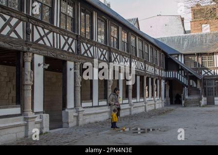 In Rouen, Frankreich, befindet sich der mittelalterliche Friedhof Aître Saint-Maclou, auf dem ein Mann und ein Kleinkind mit gelben Accessoires an einer Pfütze pausieren. Stockfoto