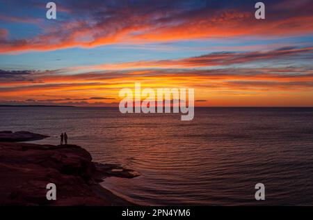 Junge Paare genießen einen bunten Sonnenuntergang am Golf von St. Lawrence Küste. Dramatischer Himmel in Rot- und Orangetönen. Ocean View Lookoff, PEI-Nationalpark. Stockfoto