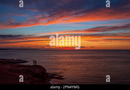 Junge Paare genießen einen bunten Sonnenuntergang am Golf von St. Lawrence Küste. Dramatischer Himmel in Rot- und Orangetönen. Ocean View Lookoff, PEI-Nationalpark. Stockfoto