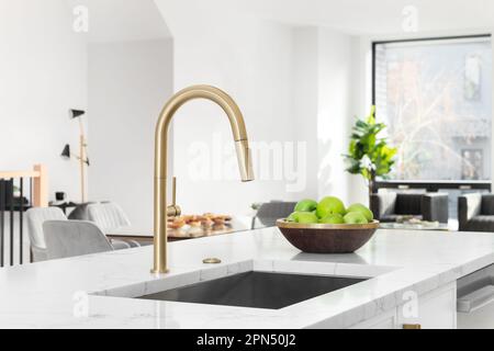 Goldene Küchen-Wasserhähne mit weißer Marmorablage, weißen Schränken und Dekorationen im Hintergrund. Stockfoto