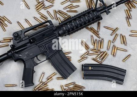 M4 Carbine und 5,56mm Schalen und Magazin mit Kugeln auf grauem Betonhintergrund Stockfoto