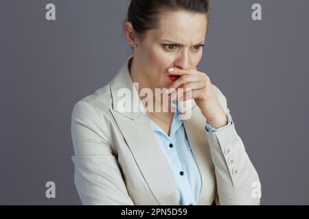 Gestresste, stilvolle Mitarbeiterin mittleren Alters in einem leichten Business-Anzug isoliert auf grauem Hintergrund. Stockfoto