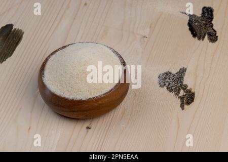 Grieß in eine runde Holzschüssel gegossen, fertig zum Kochen, einfacher Grieß mittlerer Qualität in einer Holzschüssel Stockfoto