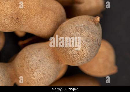 Geschlossene, lange reife Tamarindenschoten aus der Nähe, verzehrfertige ganze Tamarindenfrüchte liegen auf dem Tisch Stockfoto