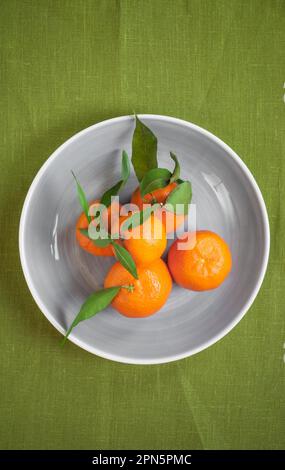 Clementine Tangerinen mit grünen Blättern auf grünem Stoff in einer grauen Schüssel Stockfoto