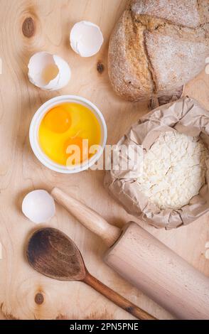 Backzutaten - Ei, Eierschale, Mehl, Walznadel, Löffel, Brot. Holzhintergrund Stockfoto