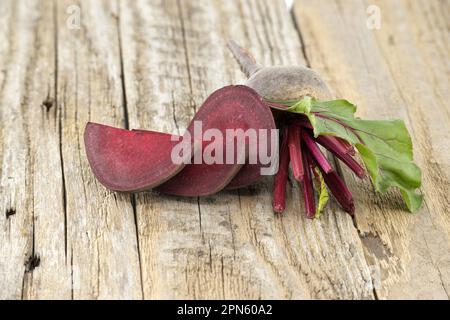 Roh geschnittene und ganze Rote Bete mit grünen Blättern auf grauem rustikalem Holzhintergrund Stockfoto