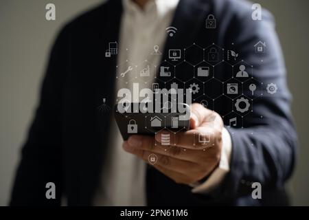 Die Hand eines Mannes hält ein Smartphone mit Mediensymbolen und -Symbolen und Anwendungssymbolen für Multitasking. Stockfoto