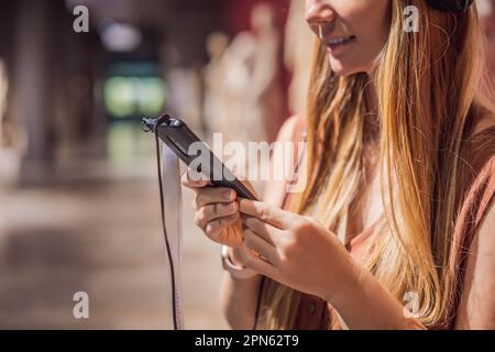 Porträt einer zeitgenössischen jungen Frau, die sich Skulpturen ansieht und in der Museumsausstellung dem Audioguide zuhört Stockfoto