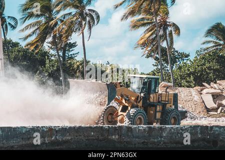 Gelber Mini-Bulldozer, der mit Stein arbeitet, Erde bewegt und Steinarbeiten durchführt. Bau eines Hotels auf der Insel. Stockfoto