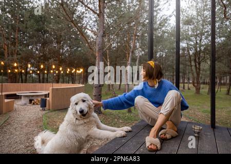 Eine Frau mit Hund ruht in der Nähe einer hölzernen Hütte in der Natur Stockfoto