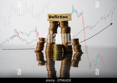 Deflationskonzept. Das Deflationswort steht auf Holzsteinen auf gestapelten Münzen Stockfoto