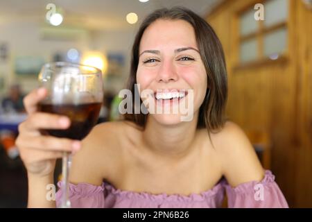 Von vorne sieht man einen glücklichen Teenager, der lacht und in einem Restaurant eine Limonade hält Stockfoto