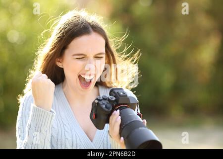 Aufgeregter Fotograf, der Fotos auf einer spiegellosen Kamera überprüft und in einem Park feiert Stockfoto