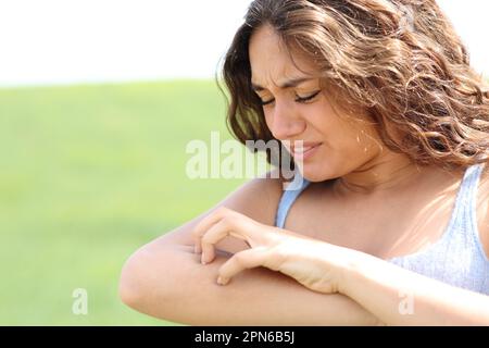 Eine Frau, die auf einem Feld einen juckenden Arm kratzt Stockfoto