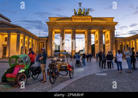 Das Brandenburger Tor beleuchtet am Abend in Berlin, der Hauptstadt Deutschlands. Lebendiger Pariser Platz mit Gruppen und geführten Fahrradtouren Stockfoto