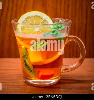 Tee im Becher mit Minze und Zitrone auf dem Hintergrund mit Holzstruktur Stockfoto