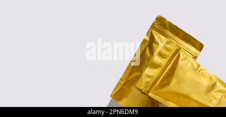 Goldene metallisierte Beutelsäcke mit Blick auf Kaffeebohnen von oben mit rauem Schatten isoliert auf weißem Hintergrund. Verpackung für Lebensmittelvorlage. Packt mit Stockfoto