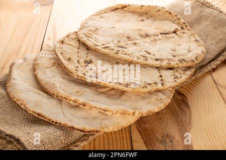 Vier gebackene Pita-Brote auf einer Jutesserviette, Nahaufnahme, auf einem Holztisch. Stockfoto