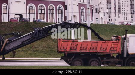 Straßenfräsmaschine entfernt alten Asphalt und lädt gefrästen Asphalt in den Muldenkipper. Reparaturprozess. Stockfoto