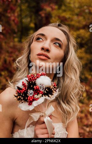 Schöne Braut mit einem Blumenstrauß in der Hand. Hochzeit im Herbst im Wald Stockfoto