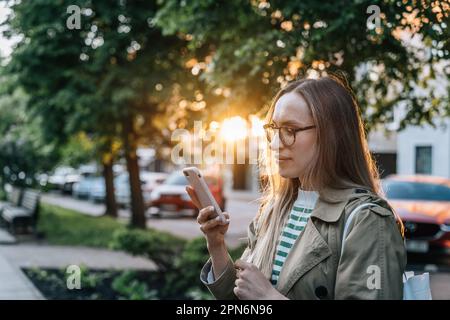 Eine Frau mit Brille benutzt abends in der Stadt ihr Smartphone Stockfoto