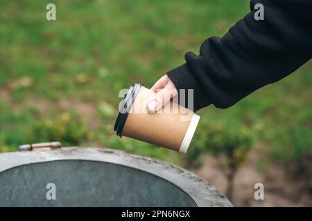 Ein Mann wirft einen Papierbecher in den Mülleimer im Park. Stockfoto
