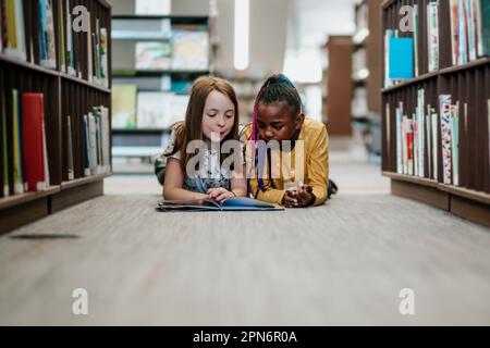 Junge Mädchen lesen drinnen zusammen ein Buch aus der Bibliothek Stockfoto