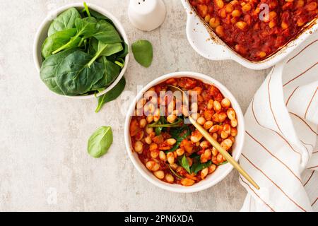 Gesundes Frühstück und Mittagessen, gedünstete weiße Bohnen mit Karotten, Zwiebeln und Tomaten mit Spinatblättern, eine Schüssel Bohnen und Spinat Stockfoto