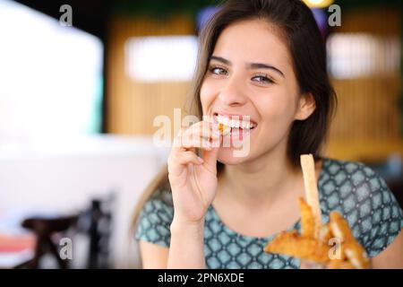 Glückliche Frau, die Hühnerfinger isst und in einem Restaurant in die Kamera schaut Stockfoto