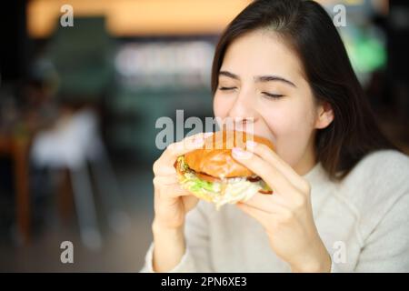 Glückliche Frau, die Burger in einem Restaurant isst Stockfoto