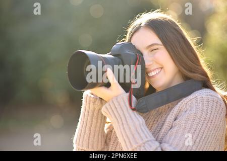 Glückliche Frau, die im Winter Fotos mit einer professionellen Kamera in einem Park macht Stockfoto