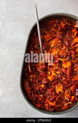 Gesundes Frühstück und Mittagessen, gedünstete rote Bohnen mit Karotten, Zwiebeln und Tomaten, Blick von oben auf eine ovale Keramikrösterei mit gedünsteten Hülsenfrüchten Stockfoto