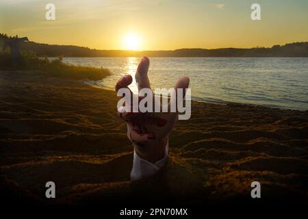 Die blutige Hand erhebt sich aus dem Sand am Strand Stockfoto