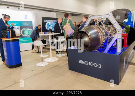 Farnborough Airport, Hampshire, Großbritannien. 17. April 2023. Im Farnborough International Exhibition & Conference Centre haben sich Branchenführer und Unternehmen der Luft- und Raumfahrtindustrie versammelt, um sich auf das Ziel zu konzentrieren, den globalen Fortschritt bis 2050 auf eine Netto-Null-Luftfahrt zu beschleunigen. Hauptredner und Ausstellungsstände unterstrichen die Entwicklungen bei Elektromotoren und alternativen Kraftstoffen als Ersatz für herkömmliche Flugzeugmotoren sowie betriebliche Veränderungen zur Verringerung der Klimaauswirkungen. Ein umgebauter Rolls-Royce AE 2100-A-Motor, aus dem der erste Motor entwickelt wird, der ausschließlich mit Wasserstoff betrieben wird. „Race to Zero“-Schriftzug Stockfoto