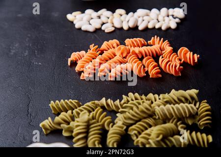 Auswahl an glutenfreien Fusilli-Nudeln aus grünen Erbsen und Karotten, Vollkornweizen auf schwarzem rustikalem Hintergrund. Bio gesunde Lebensmittel für Menschen w Stockfoto