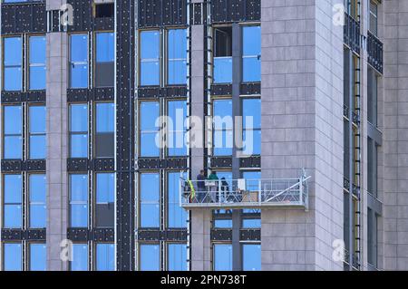 Ein Arbeiterteam auf einer Hängevorrichtung führt Kantenfassadenarbeiten in einem modernen Wohngebäude mit einer Hängeplattform durch. Stockfoto