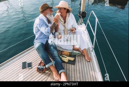 Seniorenpaar, das während der Sommerferien Champagner auf dem Segelboot trinkt - weicher Fokus auf Frauenmütze Stockfoto