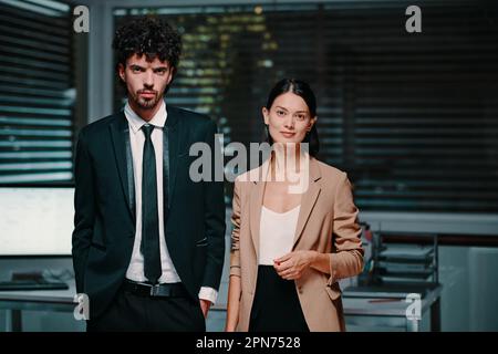Ein junges, ehrgeiziges Business-Team, das im dunklen Büro vor der Kamera steht Stockfoto