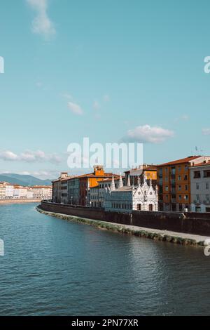 Ein wunderschöner Blick auf die Gebäude entlang des Flusses Arno in Pisa, Italien. Eine Brücke führt über den Fluss und Häuser auf beiden Seiten blicken auf das Wasser. Stockfoto