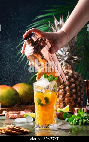Sommercocktail mit Wodka, Ananassaft, Mango, Eis. Longdrink oder kalter Mocktail. Der Barkeeper schüttelt den Kupferschüttler mit Spritzern, eingefrorener Bewegung und Stockfoto