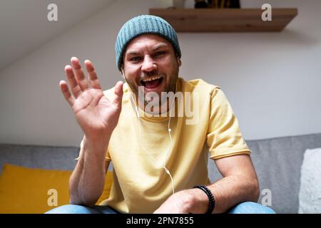 Ein Mann, der während einer Online-Besprechung lächelt und mit der Hand winkt, begrüßt Teilnehmer an Videogesprächen. Stockfoto