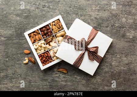 Verschiedene Nusssorten, die in einer Papierkiste auf Tischhintergrund liegen. Draufsicht. Gesundes Essen. Nahaufnahme, Kopierbereich, Draufsicht, flach liegend. Walnuss, Pistazien Stockfoto