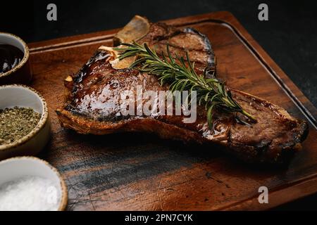 T-Bone-Steak, perfekt gegrillt mit Rosmarin und Gewürzen auf dunklem Holzbrett Stockfoto