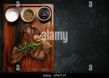 T-Bone-Steak, perfekt gegrillt mit Rosmarin und Gewürzen auf dunklem Holzbrett Stockfoto