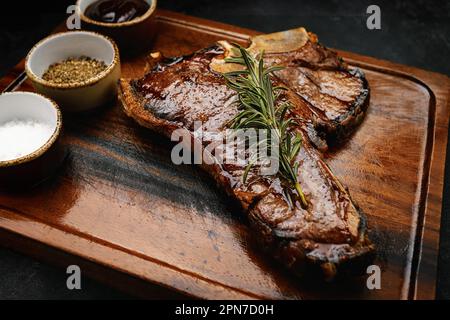 T-Bone-Steak, perfekt gegrillt mit Rosmarin und Gewürzen auf dunklem Holzbrett Stockfoto